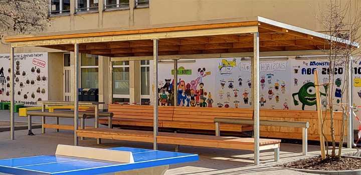 Überdachter Aufenthaltsbereich an einer Schule mit Holzbänken, Metallrahmen und Tischtennistisch, von FreiraumObjekte Ney GmbH.